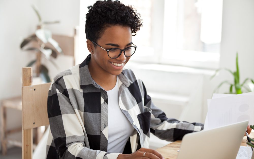 Smiling,Black,Woman,Sit,At,Desk,Working,At,Laptop,Review