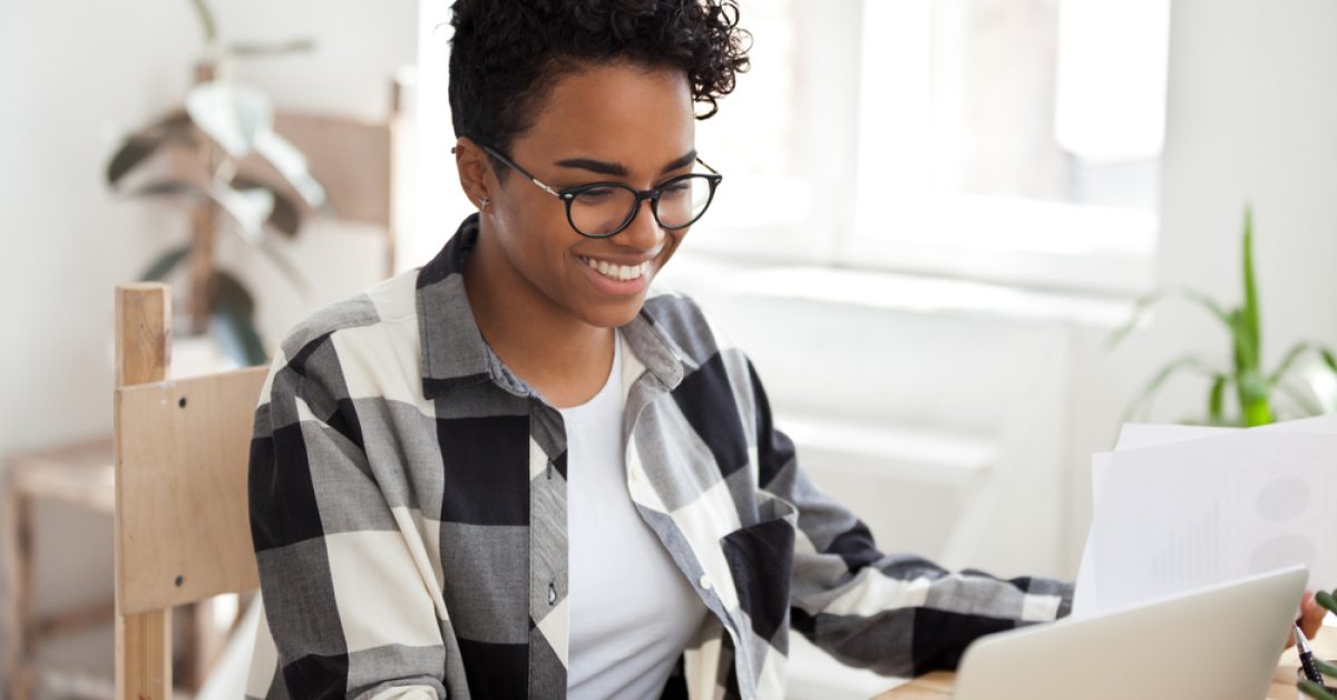 Smiling,Black,Woman,Sit,At,Desk,Working,At,Laptop,Review